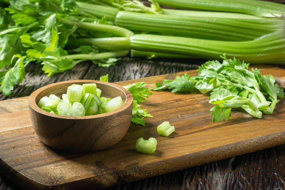 Chopped celery pieces on a wooden board with celery stalks in the background